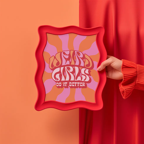 Retro-style poster with psychedelic 1970s-inspired design. Text reads "WEIRD GIRLS DO IT BETTER" in wavy, groovy lettering. Pink and orange sunburst background. Centered text surrounded by curved rays. Bold red frame with scalloped edges. Vibrant colors and playful typography create a vintage hippie vibe. Square format print with rounded corners. Perfect for fans of retro aesthetics and empowering slogans.